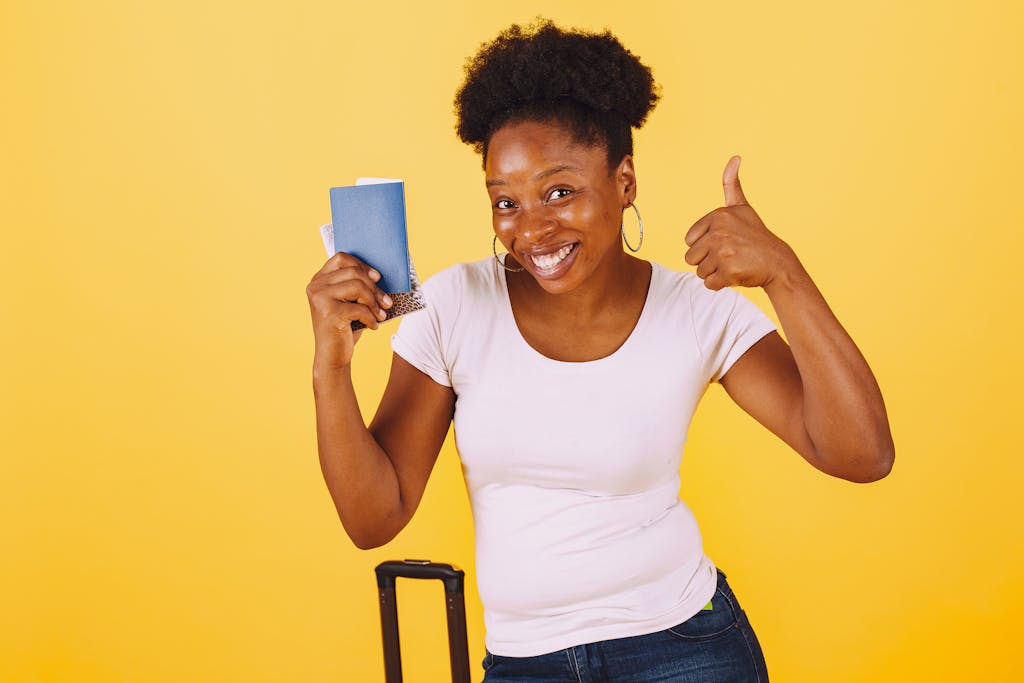 Smiling woman holding passport giving thumbs up against yellow background.